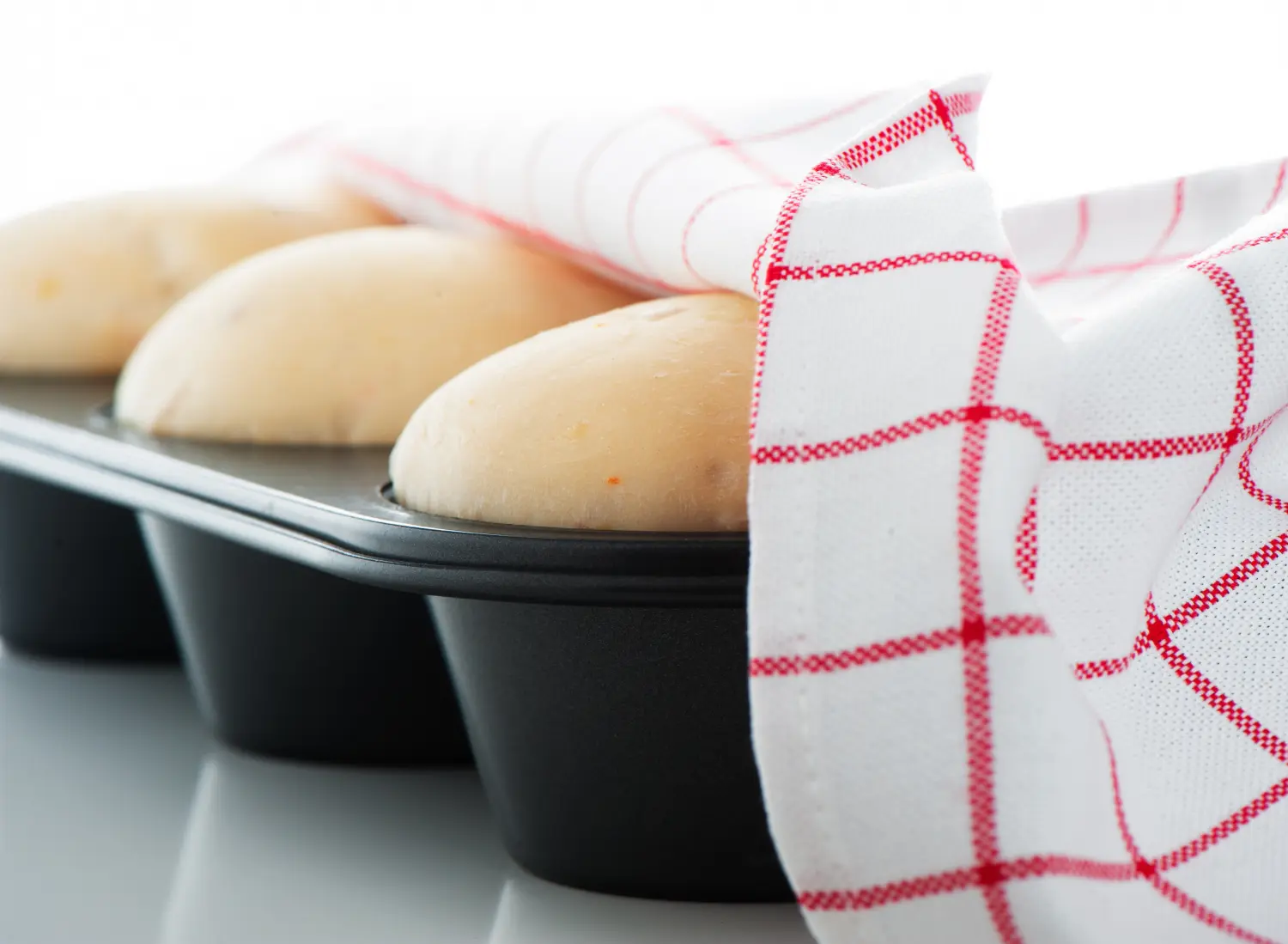 Das Bild zeigt den aufgehenden Hefeteig in einer antihaftbeschichteten Muffinform oder einem Cupcake-Blech, abgedeckt mit einem Küchentuch von Heinrich Seegers Objekttextilien GmbH